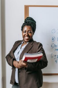 Happy black female teacher  standing with workbooks near whiteboard